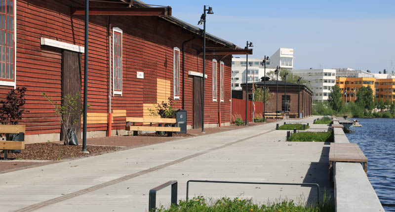 Röd träbyggnad på vänster sida. Strax utanför är det en kaj och vatten.