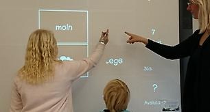 En lärare och två barn står vid en skrivtavla.