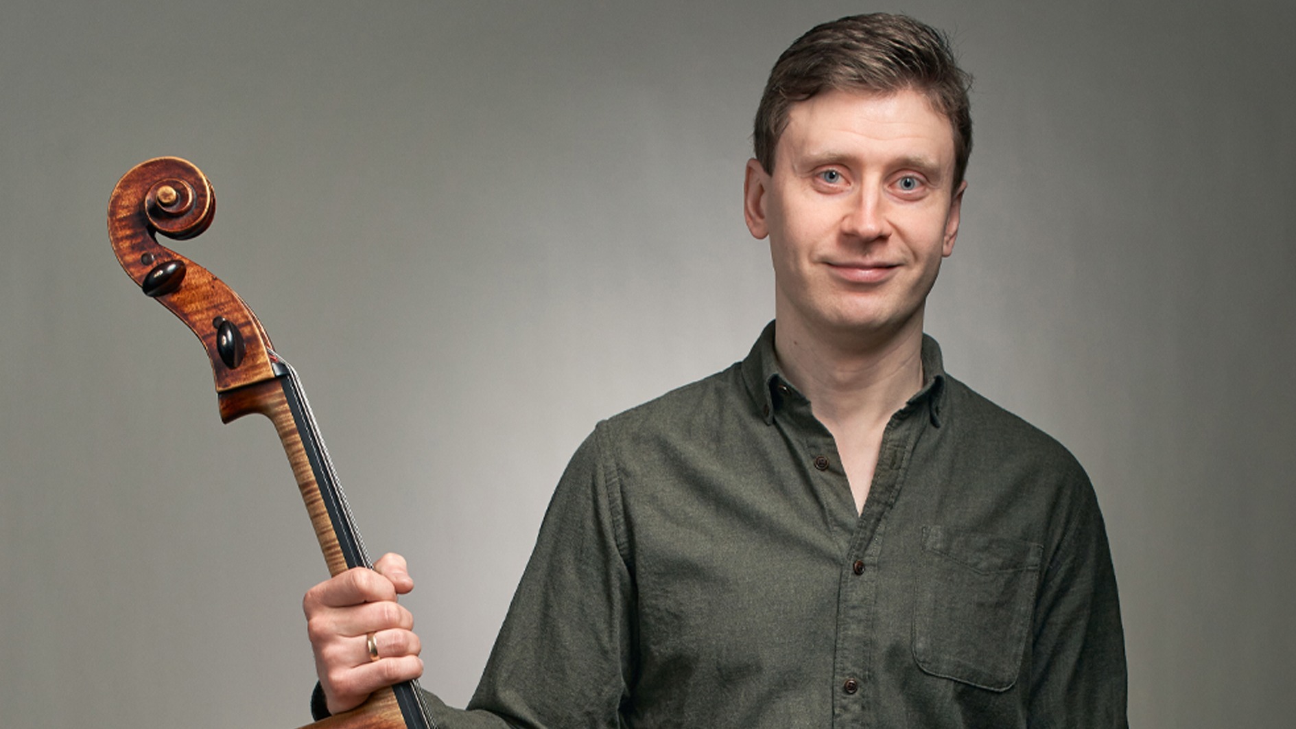 Cellisten Tuomas Lehto håller i sitt instrument och tittar in i kameran.