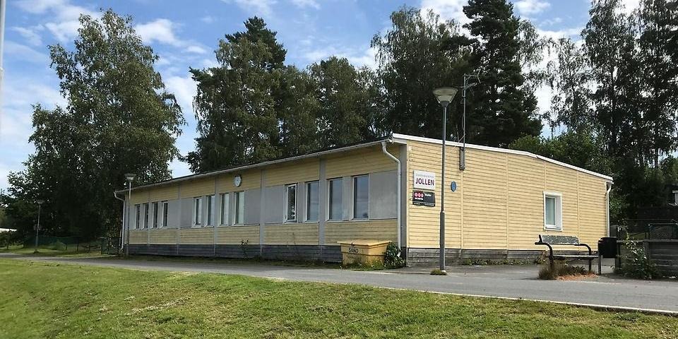 Skolbyggnaden med träd i bakgrunden och gräsmatta i förgrunden.