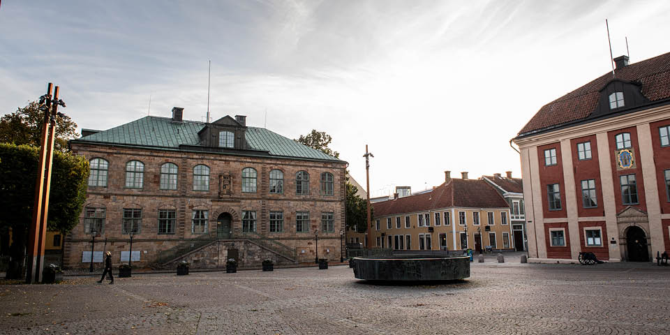 Två äldre byggnader vid en öppen torgyta med en fontän i mitten.