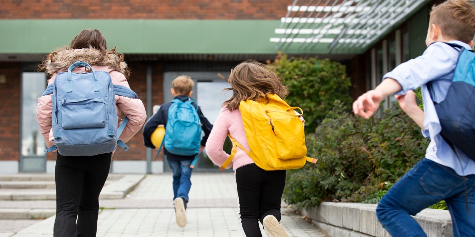 Barn med ryggsäckar springer på skolgård.