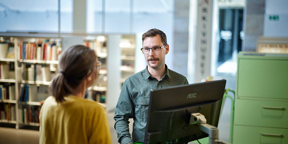 Två personer samtalar på bibliotek.