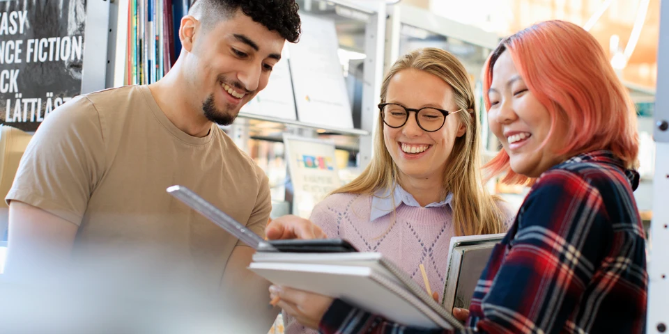 Tre glada studenter kollar i en bok.