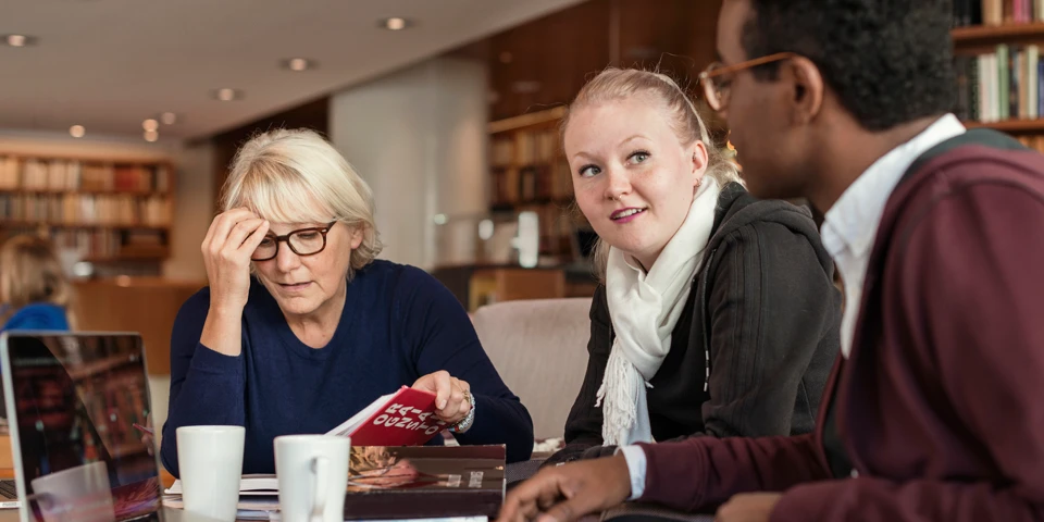 Tre personer i olika åldrar sitter och studerar på café.