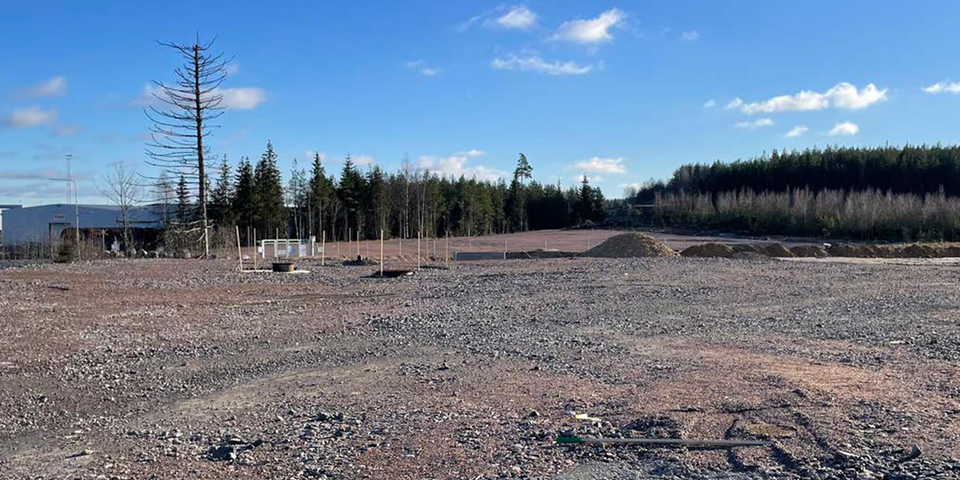 Öppet grusfält med grushögar och tallskog i bakgrunden. 