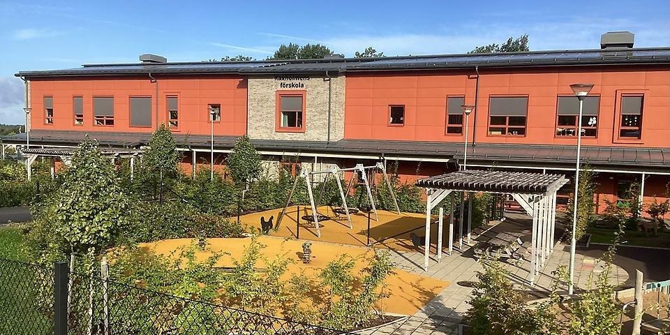 Kaxholmens förskola sedd utifrån med buskar i förgrunden och gungor i mitten.