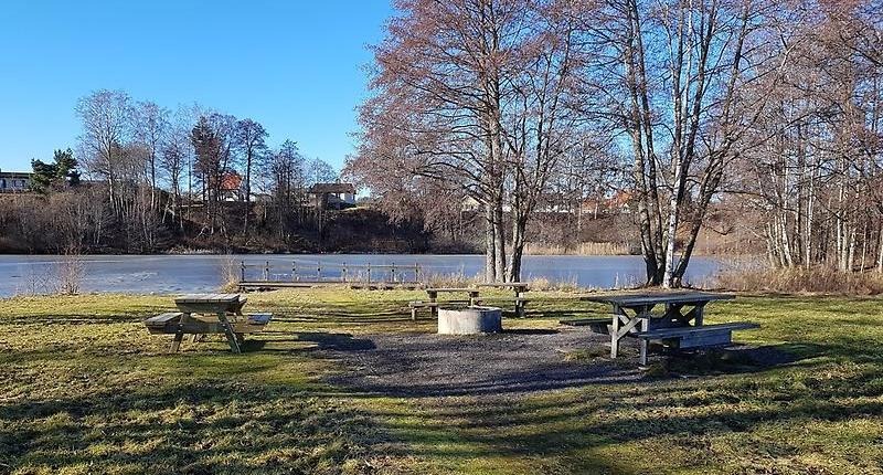 Grillplats med bänkar och bord med Attarpsdammen i bakgrunden.