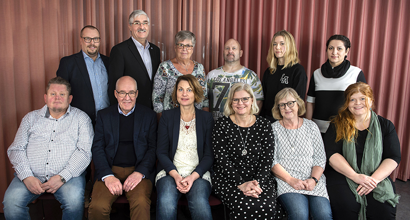 Gruppfoto på män och kvinnor framför rostrött draperi.