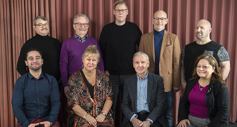 Gruppfoto på män och kvinnor framför rostrött draperi.