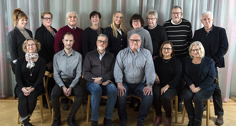 Gruppbild på män och kvinnor framför ett blågrått draperi.