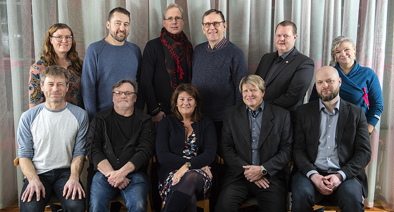 Gruppbild på män och kvinnor framför stålblått draperi.