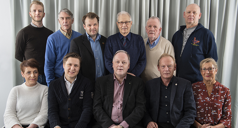 Gruppbild på män och kvinnor framför grå vägg.