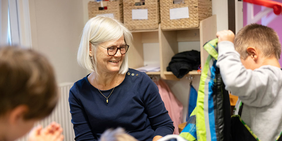 Kvinna sitter med två barn som leker runt henne. 