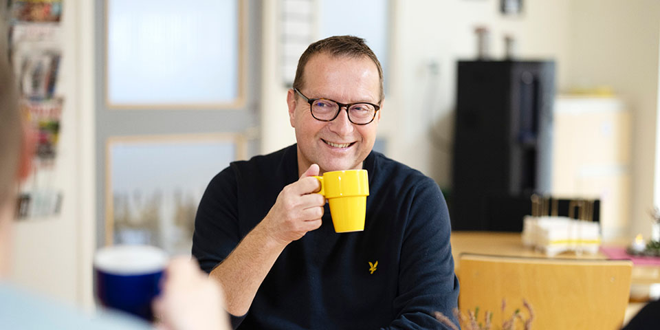 Glad person i blå skjorta dricker ur en gul kopp.
