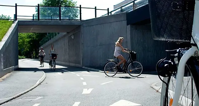 Tre cyklister som cyklar på en cykelväg under en bro.