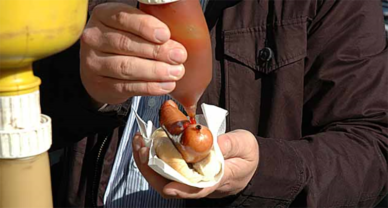En person sprutar ketchup på en korv.