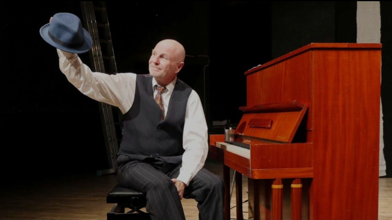 Foto på Sven Kristersson med hatten i handen vid ett piano.
