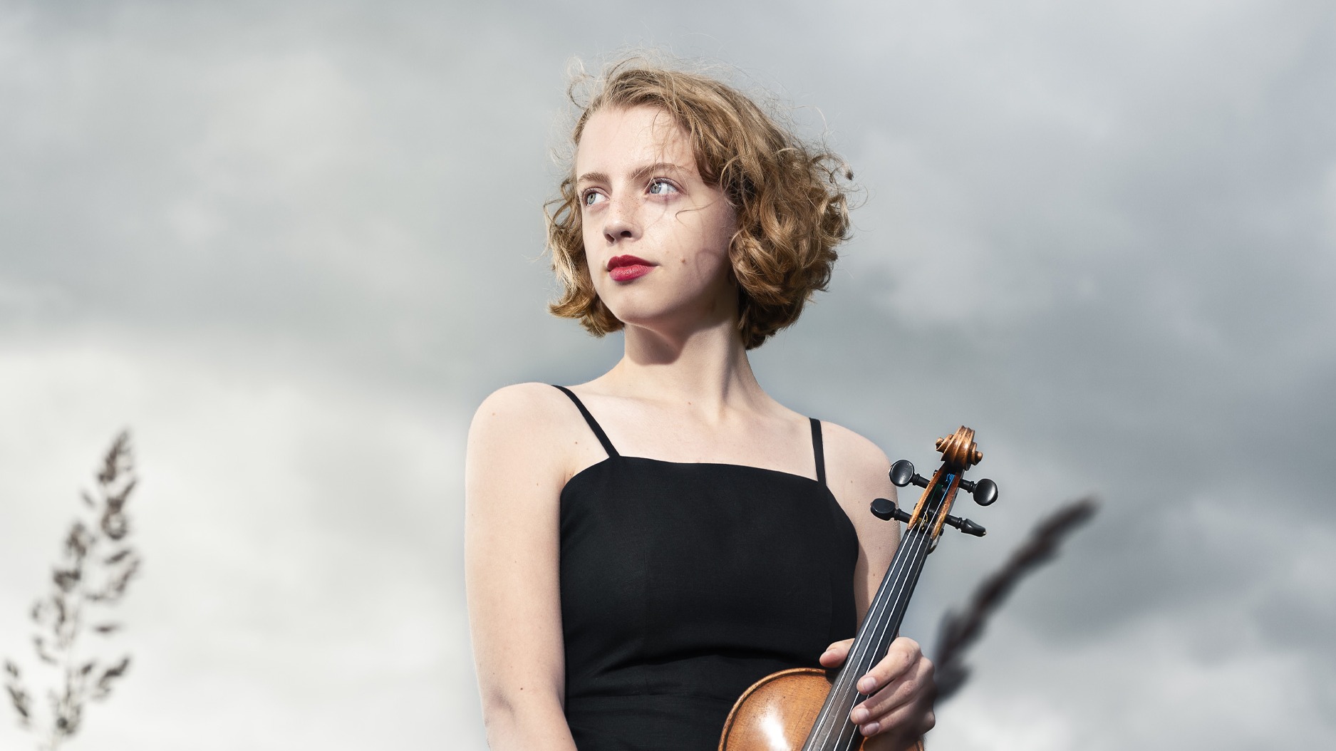 Violinisten Alva Holm står på en äng med sin violin och blickar ut