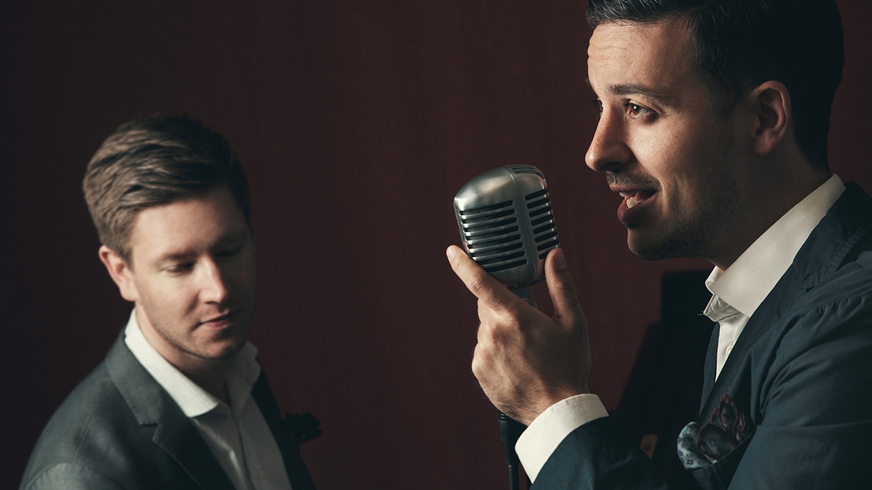 Föreställningens medverkande Jakob Sollevi och Filip Ekestubbe. Båda är iförda kostym och en av dem sjunger i en retro-inspirerad mikrofon.