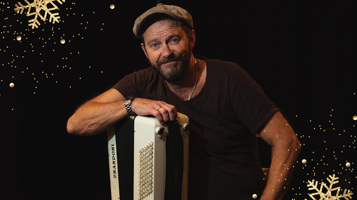 Bengan Janson håller i sitt dragspel och tittar in i kameran. Guldiga snöflingor syns.