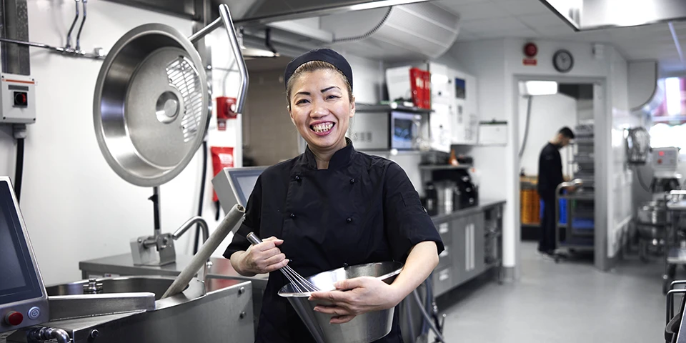 En glad kvinna i svarta restaurangkläder som rör i en silverfärgad skål.
