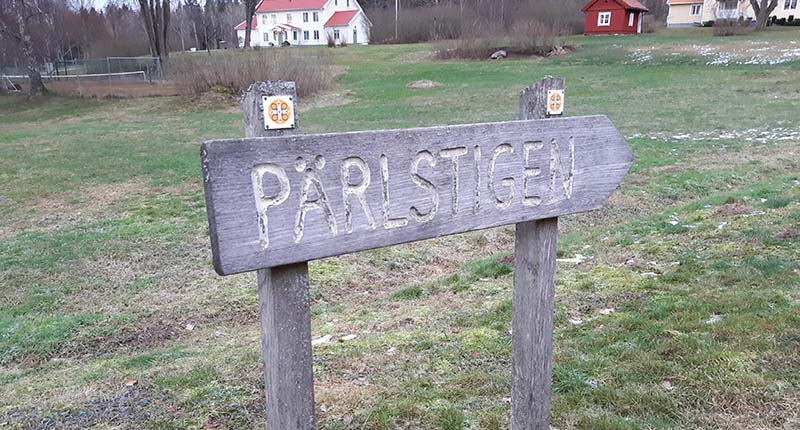 En träskylt med inristningen "Pärlstigen" står på en grön gräsmatta.