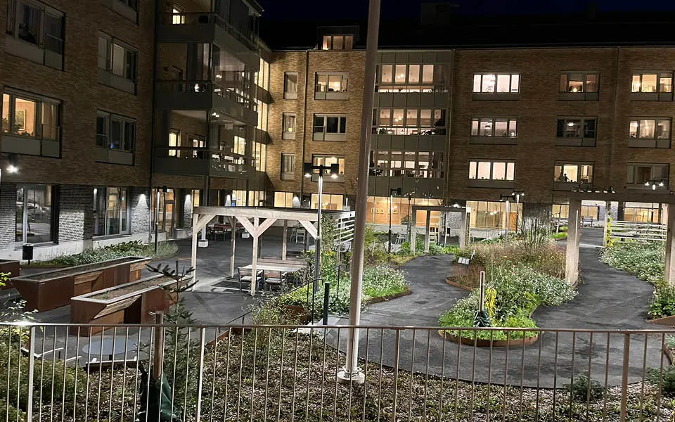 En innergård med flerbostadshus omkring, med grönska, sittplatser och belysning.