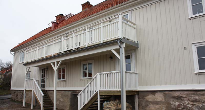 Vit långsmal träbyggnad i två plan med stor balkong.