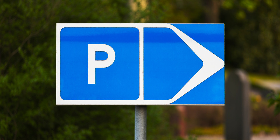 En blå parkeringsskylt med vit text och symboler, som pekar mot parkeringsyta.