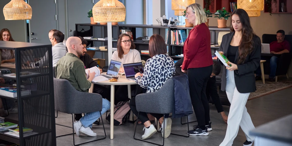 Flera personer sitter och studerar vid ett bord och diskuterar något. 
