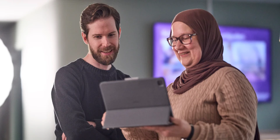 Kvinna visar något på en ipad för en man. 