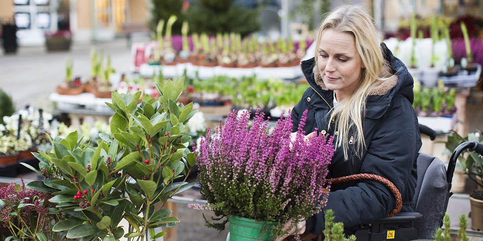 En person som sitter i rullstol på ett torg med blomster- och växtförsäljning.