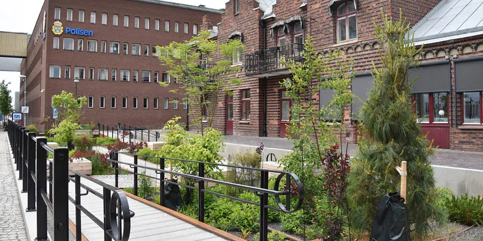 Park med gröna inslag framför mörka tegelbyggnader.