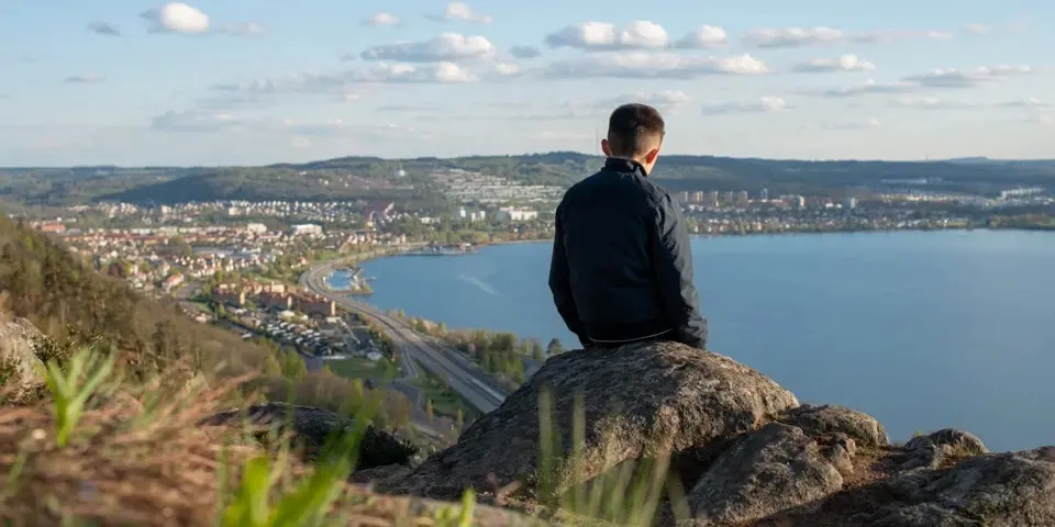 En man sitter på en sten vid en utsiktsplats och ser ut över Vättern.