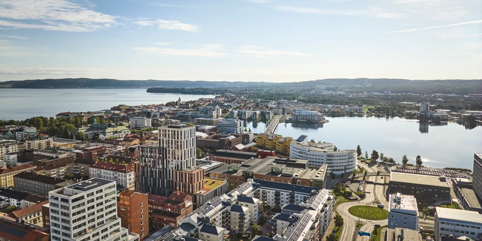 Flygfoto över Jönköpings city med en blandning av moderna och traditionella byggnader, omgiven av vatten och grönområden. Vättern och Munksjön syns vid stadens kant under en klar himmel med några moln.