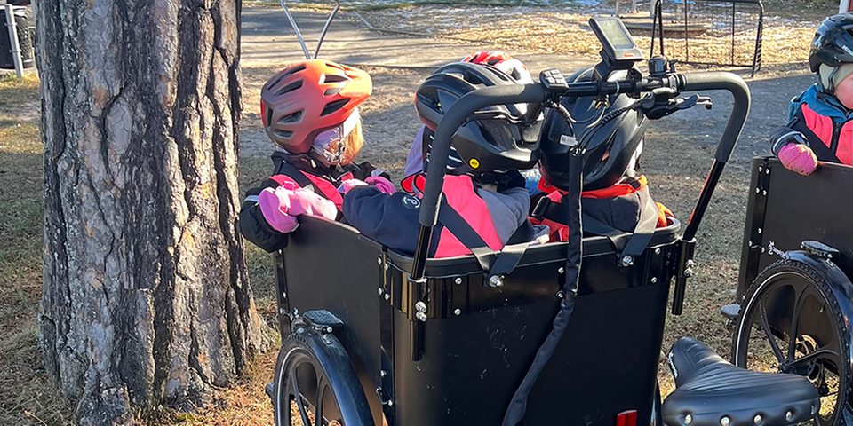 Yngre barn som sitter i en cykelkärra med hjälmar.